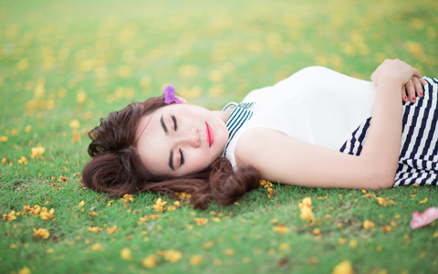 Relaxed woman laying in spring grass with flowers in her hair