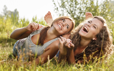 two happy girlfriends smiling and rolling around in the grass