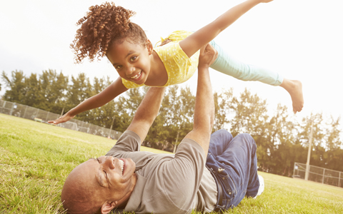 father lifting his daughter over his head, happy and playing in the park