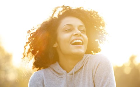 young woman with curly hair smiling at sunset