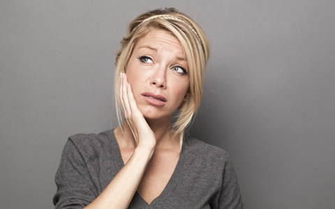 woman with hand to her mouth, wondering what her tooth pain could mean