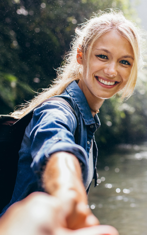 young blonde woman extending her hand and reaching for someone to go on an adventure with her outside