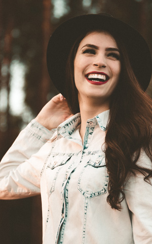 Woman in denim shirt and black hat, smiliting outdoors