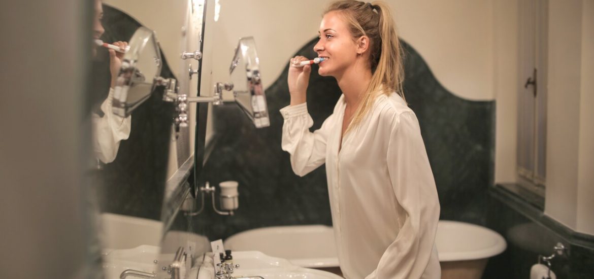 woman brushing teeth in front of a mirror