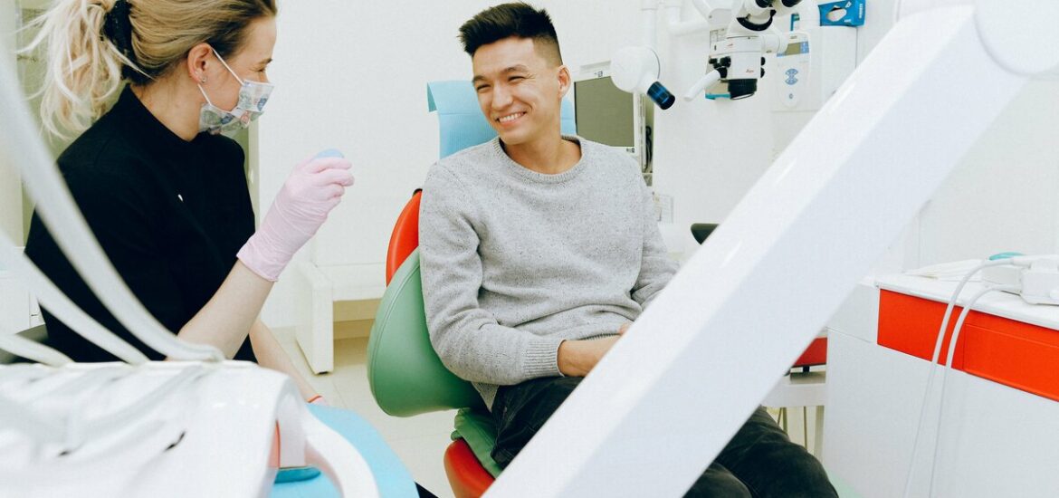 man in a dental chair smiling next to a female hygienist