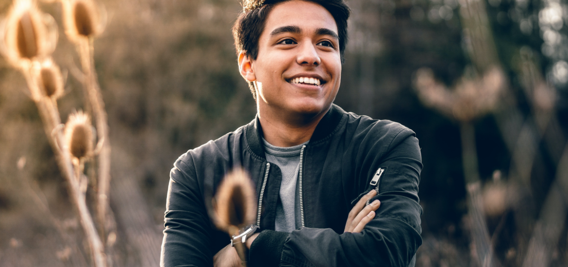 Young man crossing his arms over his chest and smiling while standing in a field