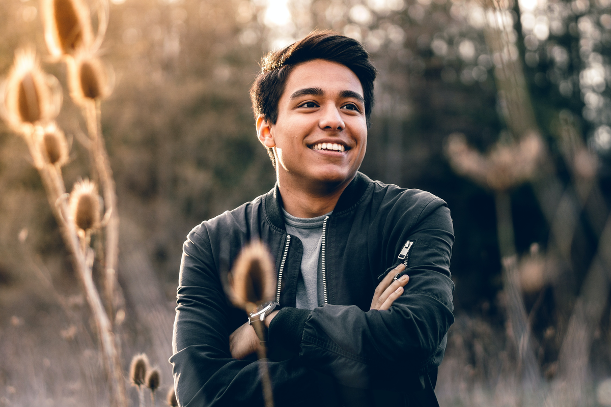Young man crossing his arms over his chest and smiling while standing in a field